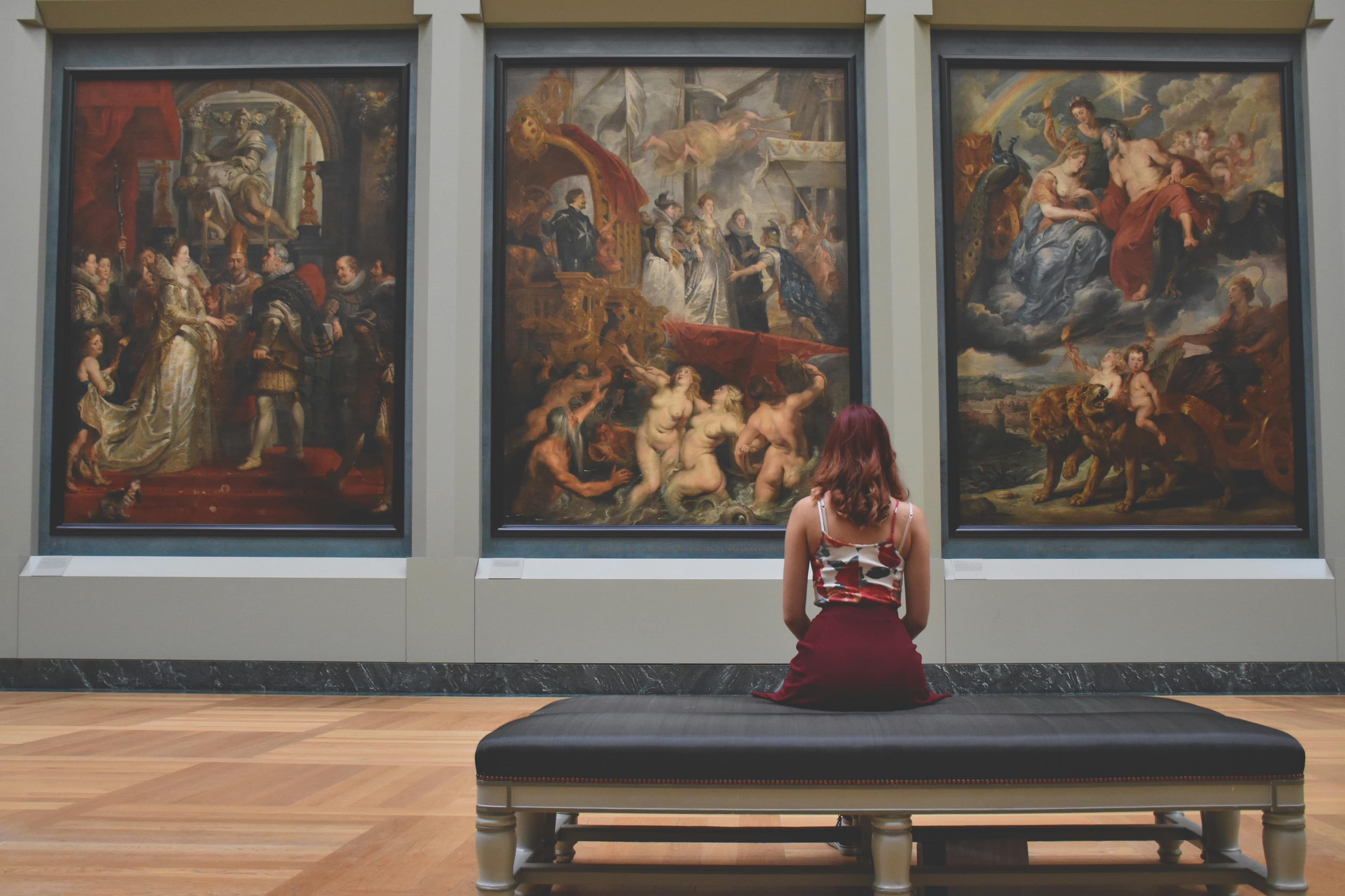 A woman seated before three paintings in a museum gallery