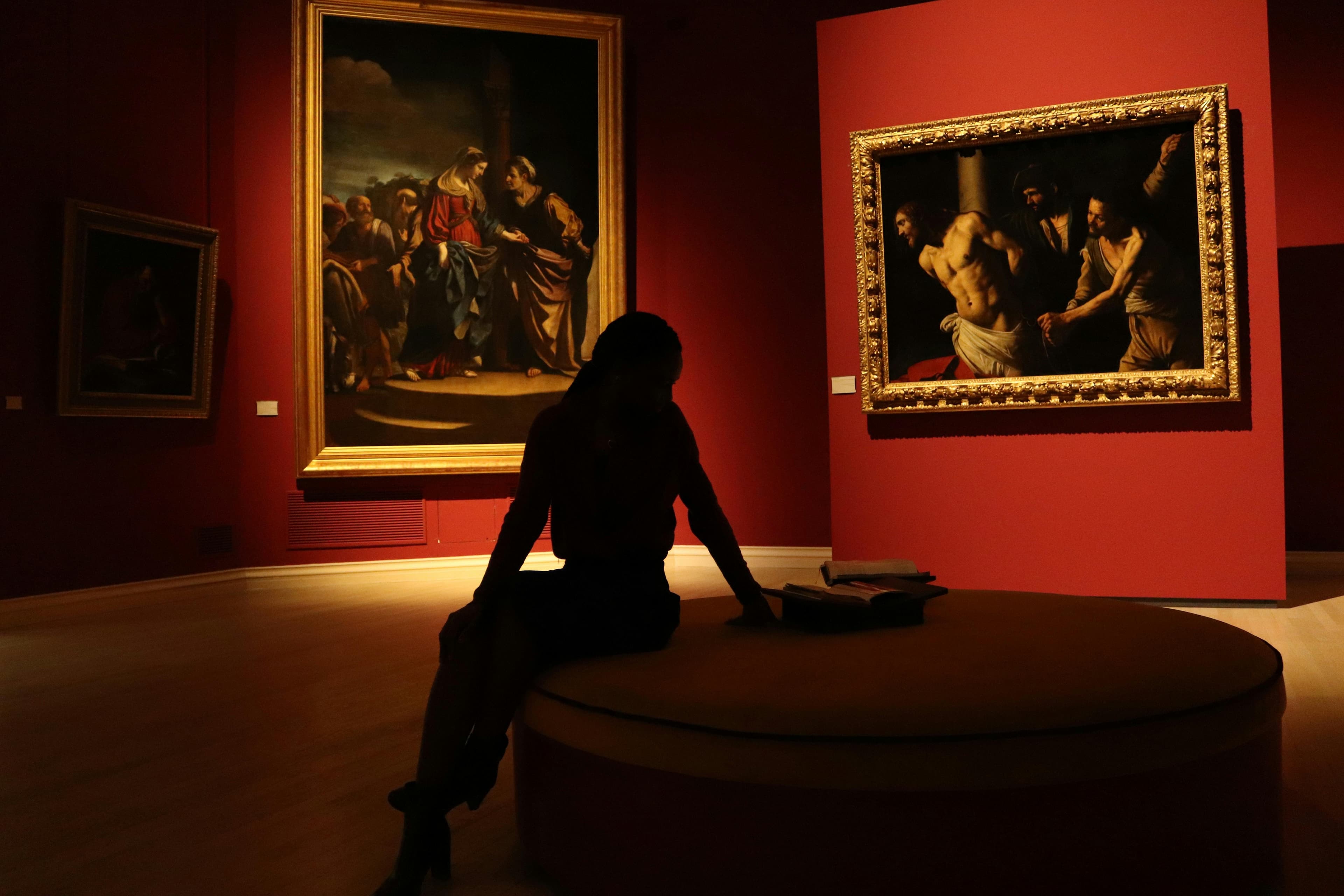 A silhouetted visitor seated in a red museum gallery